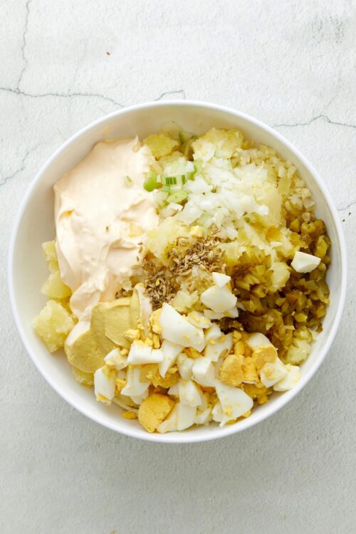 Creamy potato salad with chopped boiled eggs, celery, onions, pickles, and mayonnaise in a white bowl.