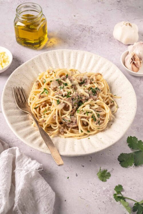Creamy tuna pasta spaghetti with garlic and herbs on a white plate.