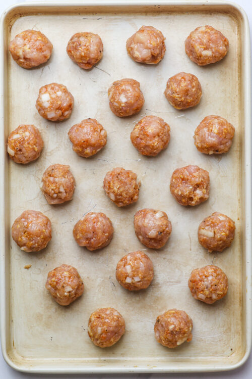 Golden baked chicken meatballs on a baking sheet, ready for oven.