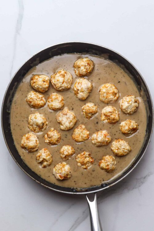 Creamy mushroom gravy with meatballs cooking in a skillet.