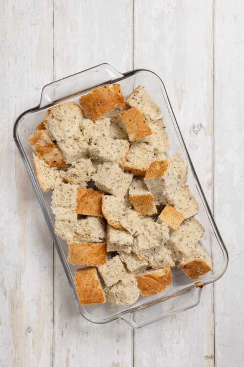 Homemade croutons in a glass baking dish on a rustic white wooden background.