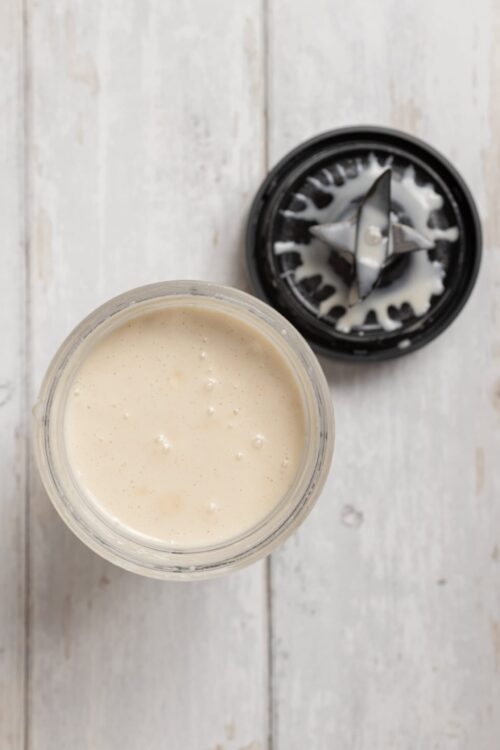 Creamy homemade vanilla bean coffee creamer in a glass jar with blender attachment on a white wooden surface.