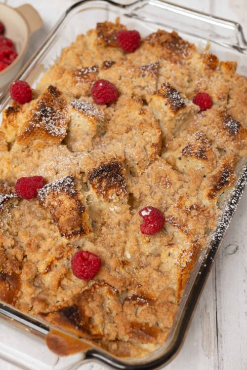 Baked raspberry apple crisp in a glass baking dish with fresh raspberries on top.
