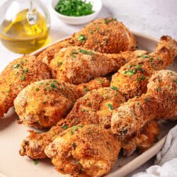 Crispy baked chicken drumsticks and thighs on a white platter with herbs.
