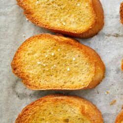 Golden toasted garlic bread slices on parchment paper.
