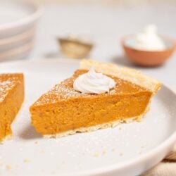 Rich pumpkin pie slice topped with whipped cream on a white plate.