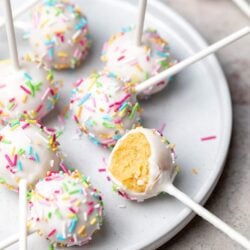 Colorful birthday cake pops with rainbow sprinkles on a white plate.