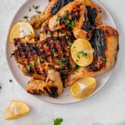 Juicy grilled lemon chicken with charred skin and fresh herbs on a white plate.