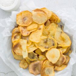 Crispy homemade potato chips flavored with sea salt on white parchment paper.