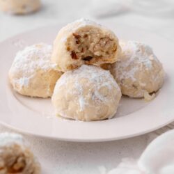 Buttery cookie dough balls coated in powdered sugar with a glimpse of chopped nuts inside, perfect for holiday treats or baking recipes.