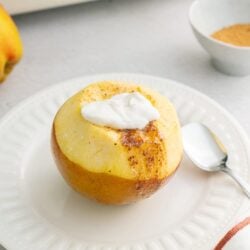 Baked Bree apple with cinnamon and whipped cream on a white plate, cozy kitchen setting.