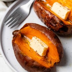 Roasted sweet potato halves with butter and black pepper on a white plate.
