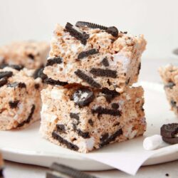Oreo ice cream cake bars stacked on white plate with Oreo pieces around.