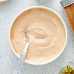 Creamy homemade blue cheese dressing in a white bowl, with chopped pickles and seasonings around it.