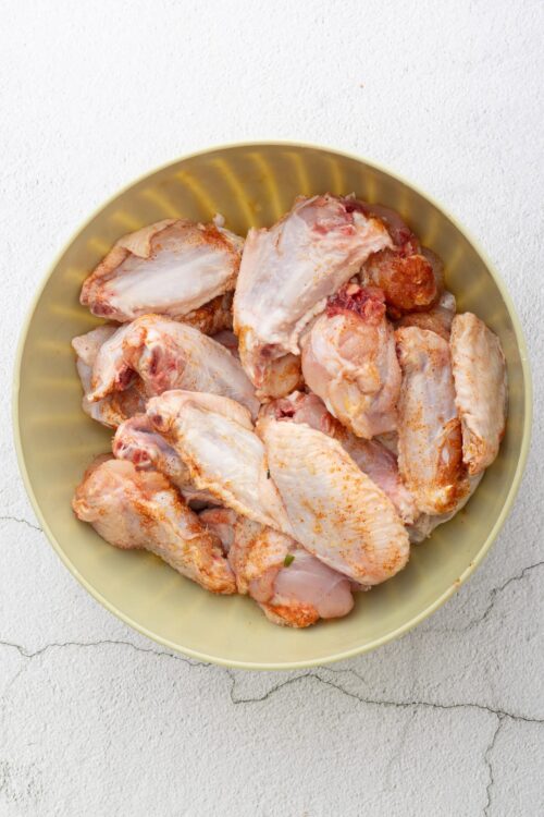 Boneless chicken thighs seasoned with spices in a yellow bowl for baking.