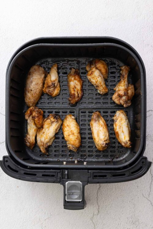 Crispy air fryer chicken wings cooked in a black air fryer basket on a white textured surface.