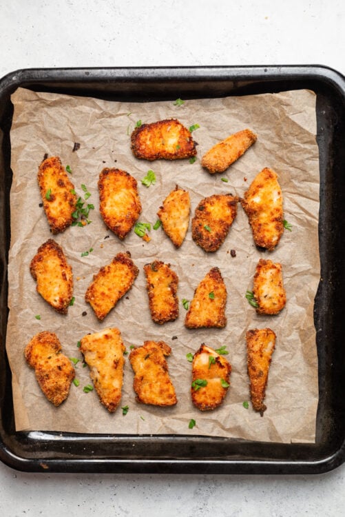 Crispy baked chicken tenders on parchment paper with fresh herbs.