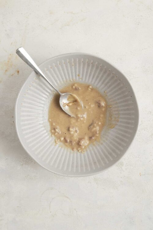Creamy sausage gravy in a white bowl with a silver spoon, perfect for breakfast comfort food.