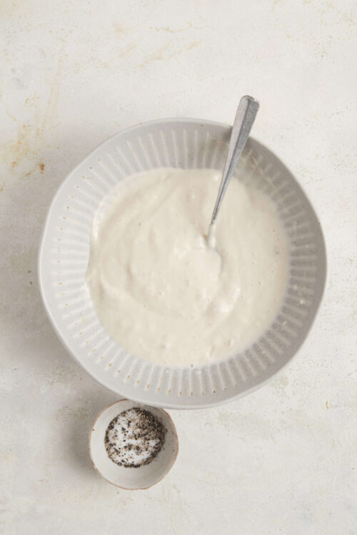 Creamy homemade ranch dressing in a white bowl with a spoon on a textured white surface.