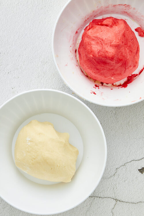 Soft pink and yellow dough balls in white bowls for baking recipes.