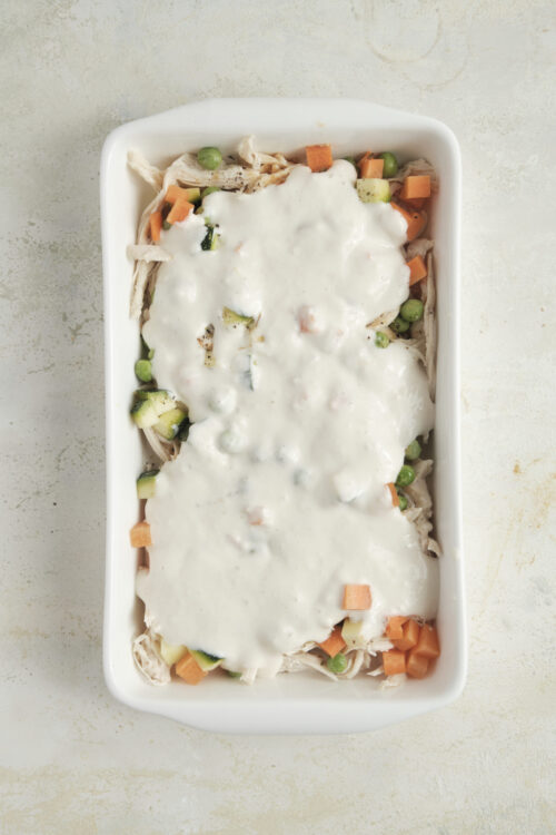 Creamy chicken pot pie in a white baking dish with mixed vegetables and rich white sauce.
