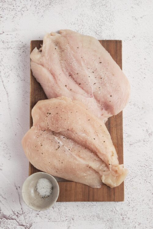 Juice chicken breasts seasoned with salt and pepper on a wooden board.
