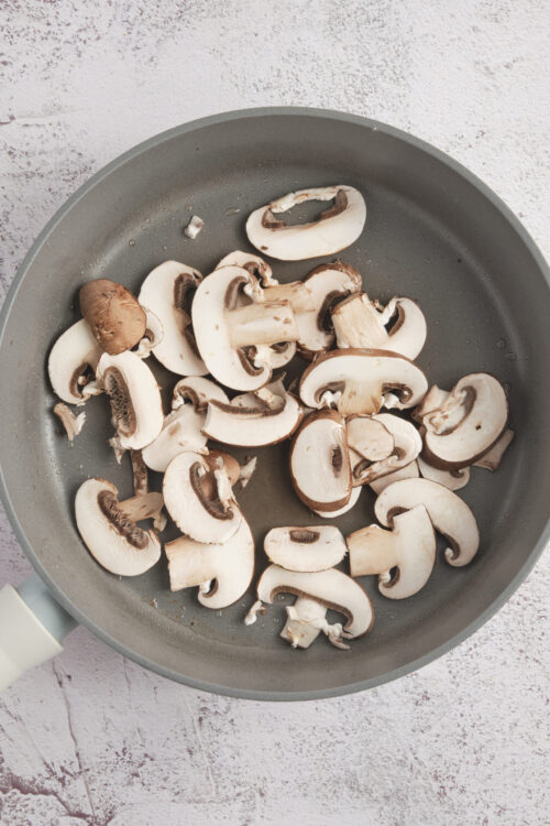 Sliced fresh white mushrooms in a gray frying pan for cooking or sautéing.