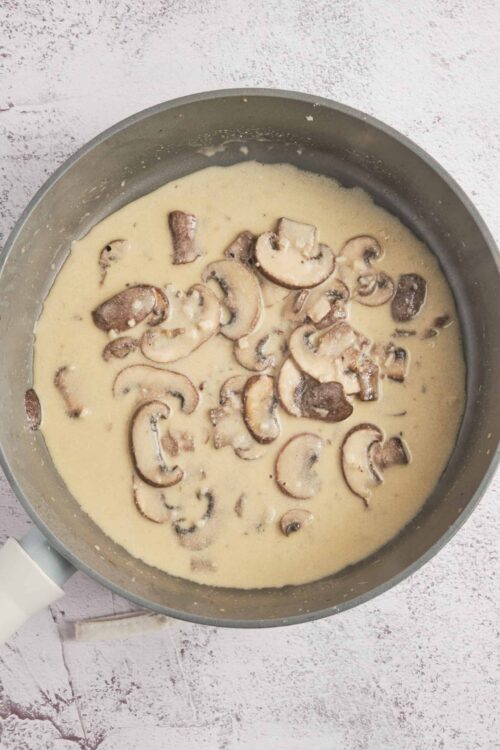 Creamy mushroom sauce cooking in a skillet with sliced mushrooms.