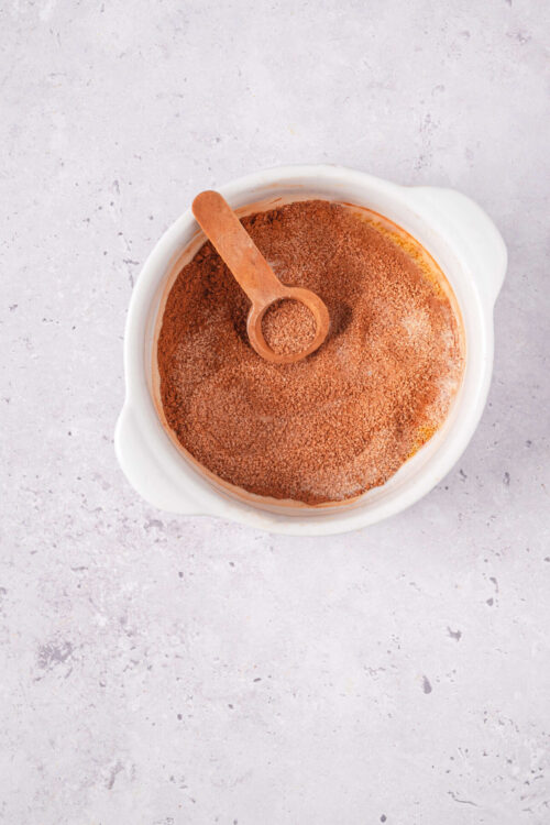 Ground cinnamon in a white bowl with a wooden spoon for baking recipes.