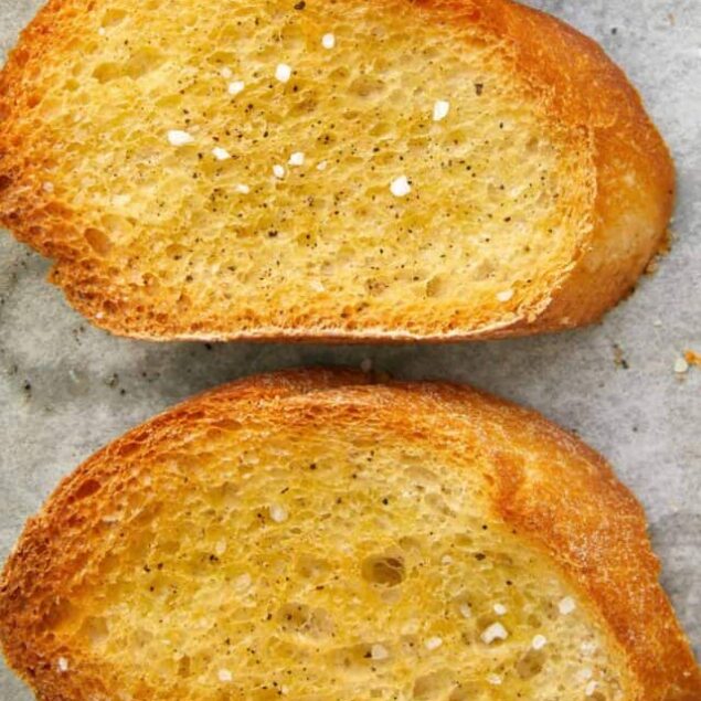 Golden toasted garlic bread slices on parchment paper.