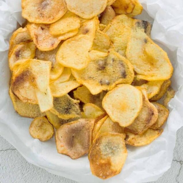 Crispy homemade potato chips flavored with sea salt on white parchment paper.
