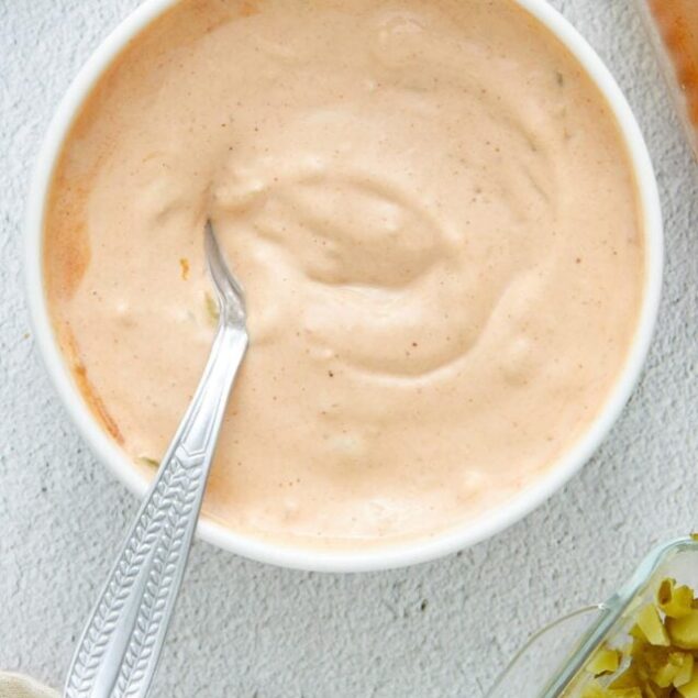 Creamy homemade blue cheese dressing in a white bowl, with chopped pickles and seasonings around it.