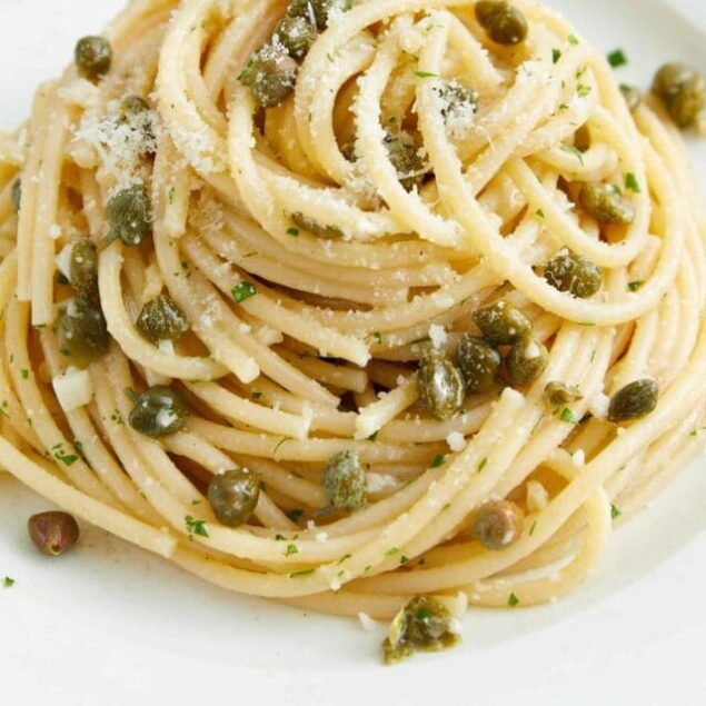 Creamy pasta dish with capers and grated cheese on a white plate.