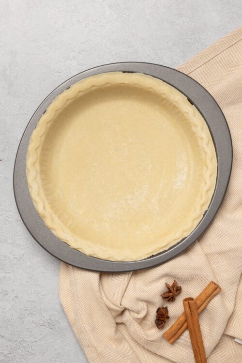 Golden pie crust ready for baking, with spices on the side.