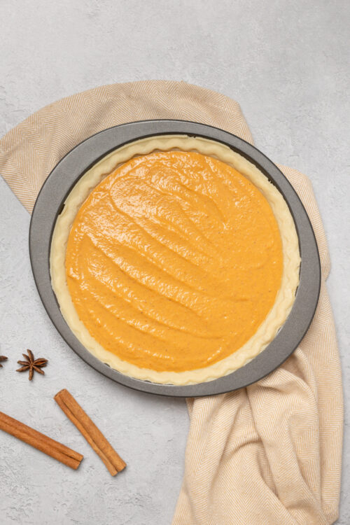 Sweet potato pie in a pie dish with spices on a textured background.
