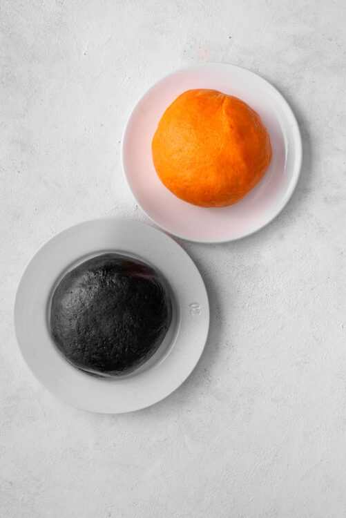 Fresh orange and black garlic on white plates, healthy food ingredients for cooking or baking.