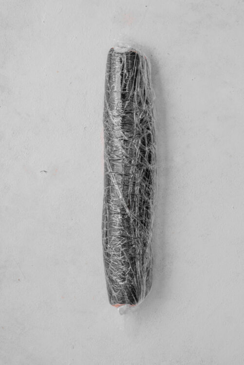 Unwrapped chocolate and vanilla baked goods wrapped in plastic, on a plain white surface.