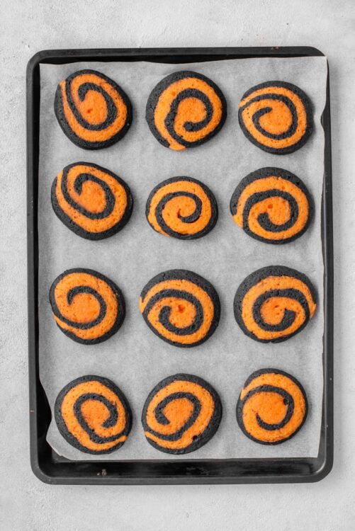 Bright orange and black swirl cookies on baking sheet with parchment paper.