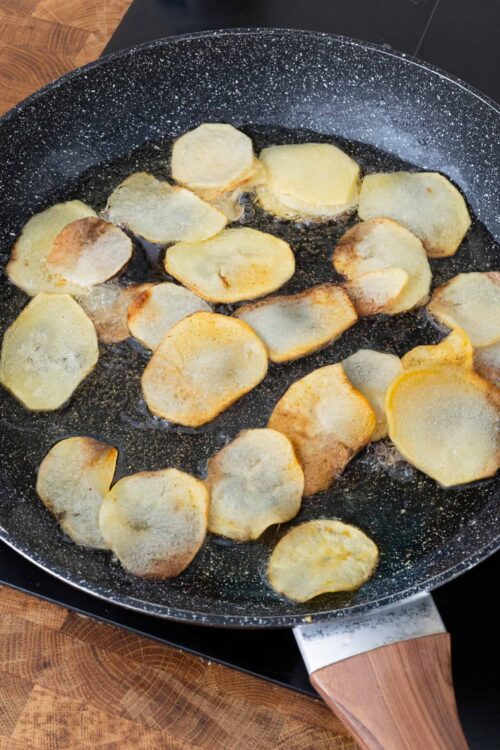 Golden crispy potato chips frying in a non-stick skillet.