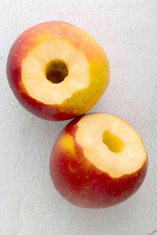 Sweet red and yellow apple with core removed, on white textured background.