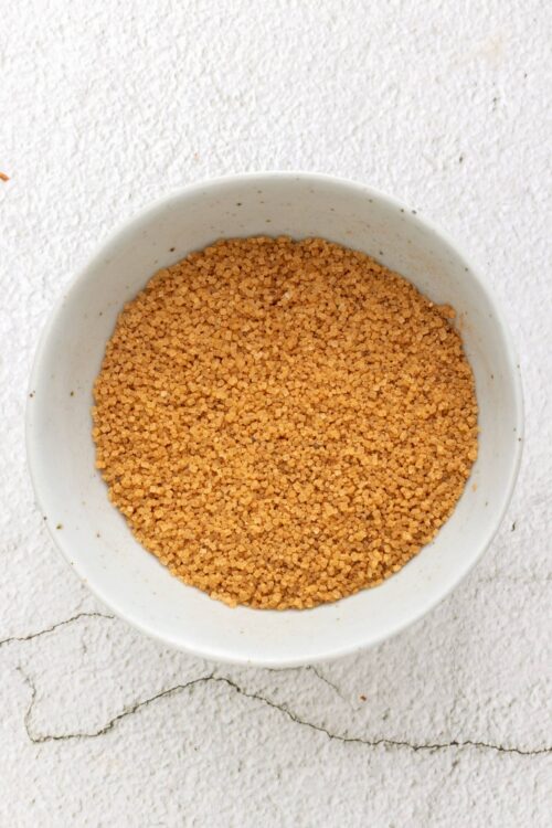 Breadcrumbs in a white bowl on a textured white surface.