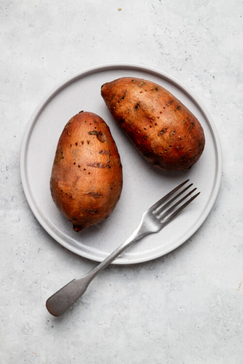 Sweet potatoes on white plate with fork, healthy baked sweet potato side dish, fresh root vegetables.