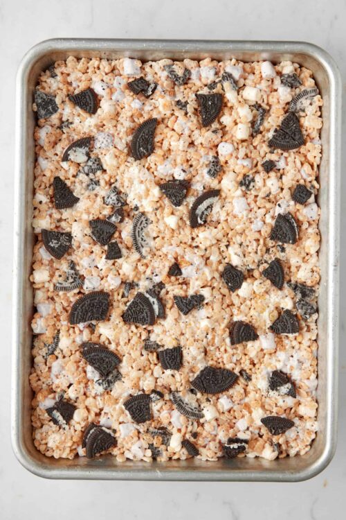Oreo rice-crispie treat mixture in a baking pan with crushed cookies and marshmallows.