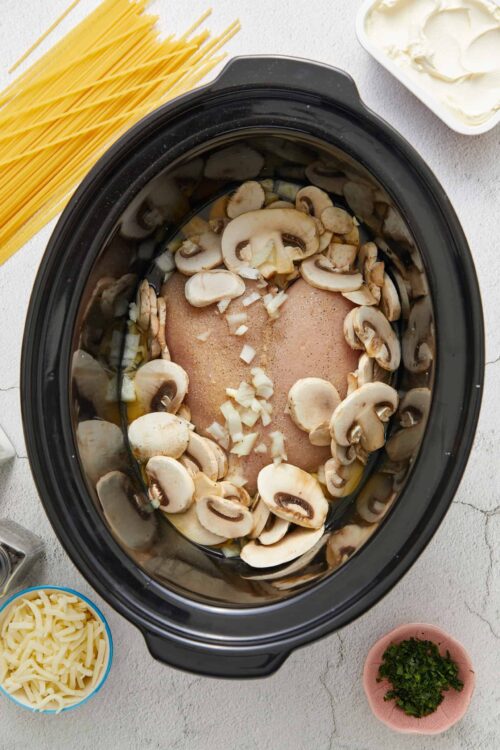 Sliced mushrooms and seasoned chicken in a slow cooker for a delicious mushroom chicken recipe.