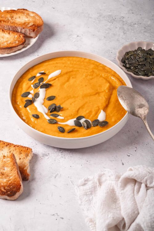 Creamy pumpkin soup with pumpkin seeds and a swirl of sour cream, served with toasted bread slices.