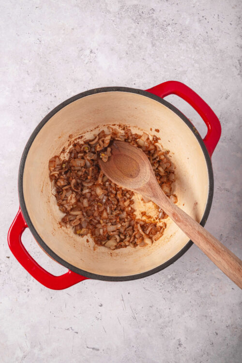 Sautéed onions and spices in a red Dutch oven, cooking for a savory dish.