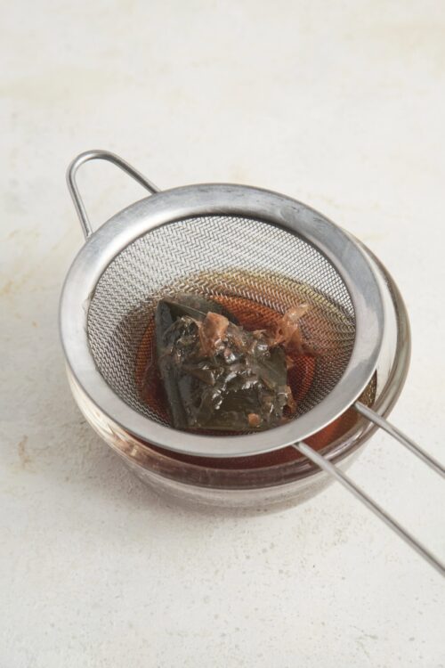 Steeping tea leaves in hot water using a fine mesh tea strainer.