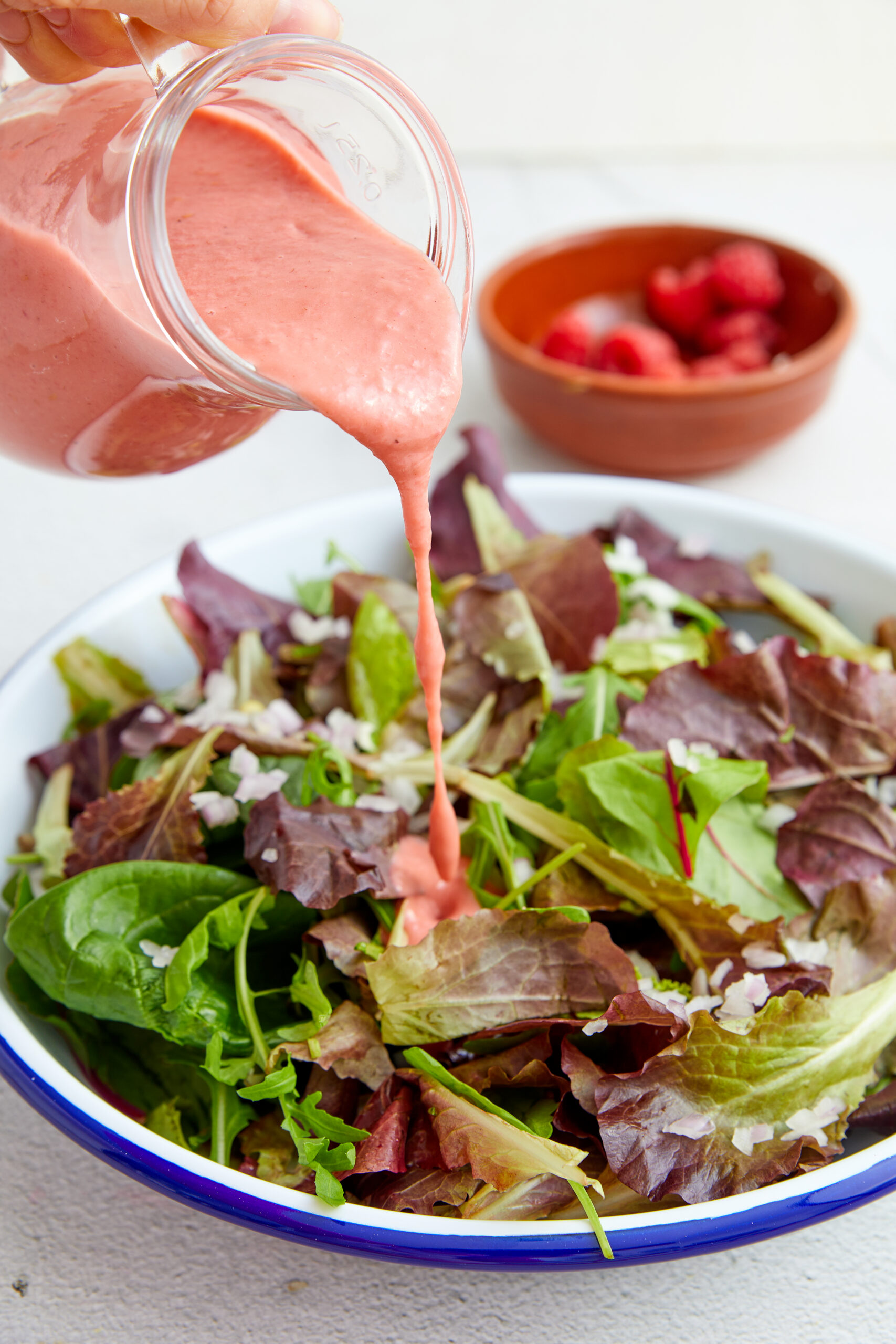 Raspberry Vinaigrette in a small glass pitcher being poured on a salad